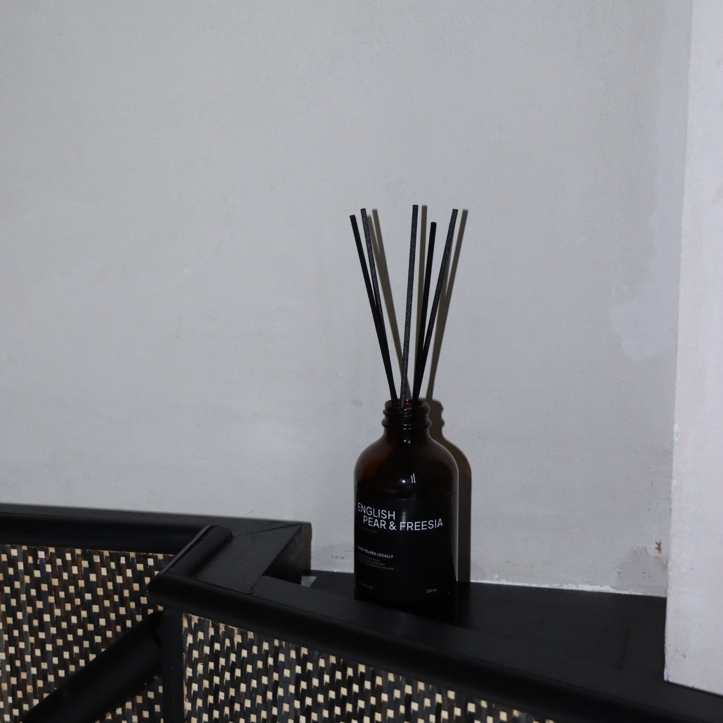 Dark brown diffuser bottle with sticks on a black surface against a white wall