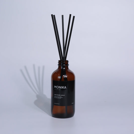 Reed diffuser with a brown bottle and black sticks on a white background