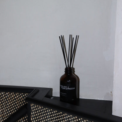 Dark brown diffuser bottle with sticks on a black surface against a white wall