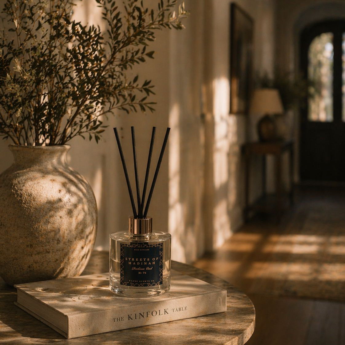 A diffuser bottle on a book with a vase and plant in the background
