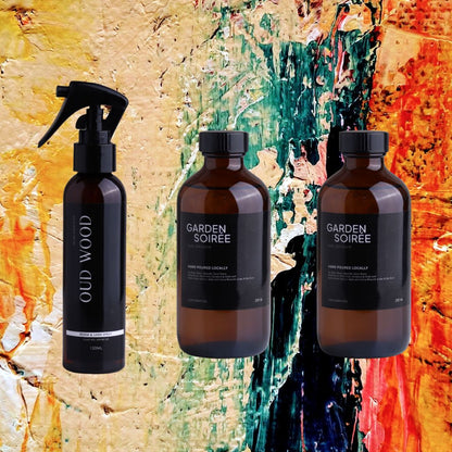 Three brown bottles with black caps labeled 'Garden Soiree' and 'Oud' against a colorful abstract background.