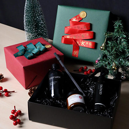 Gift box with a green ribbon, black box with bottles, and Christmas trees on a dark background