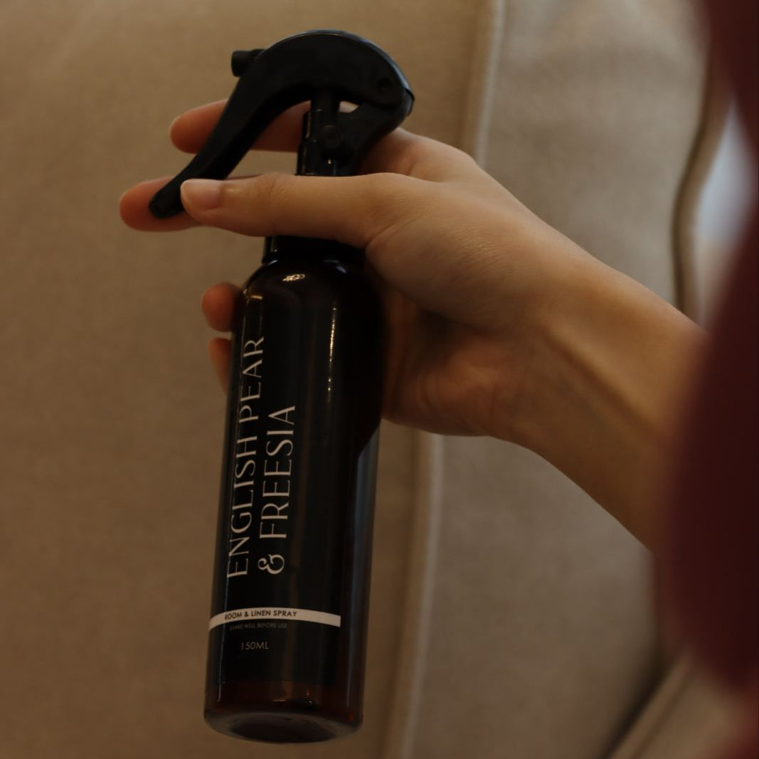 Hand holding a black spray bottle labeled 'Englisheaven & Freesia' against a beige background.